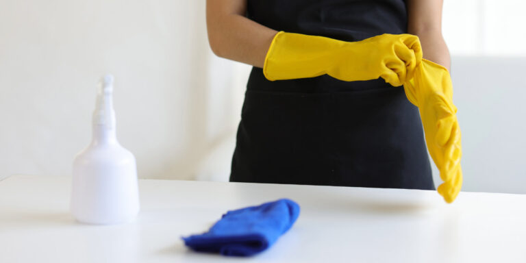 Person wearing yellow gloves preparing for maintenance cleaning with cleaning supplies on a table