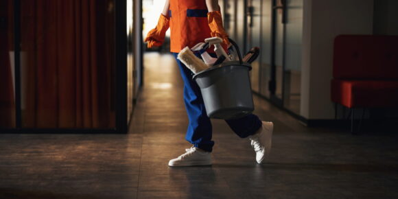 Person in uniform holding cleaning supplies bucket in office hallway as part of day porter checklist duties