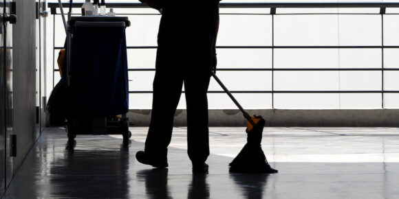Silhouette of a cleaning worker mopping a shiny floor with cleaning cart nearby, illustrating porter vs janitor roles in facility maintenance