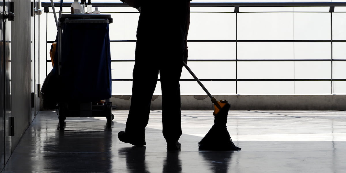 Silhouette of a cleaning worker mopping a shiny floor with cleaning cart nearby, illustrating porter vs janitor roles in facility maintenance