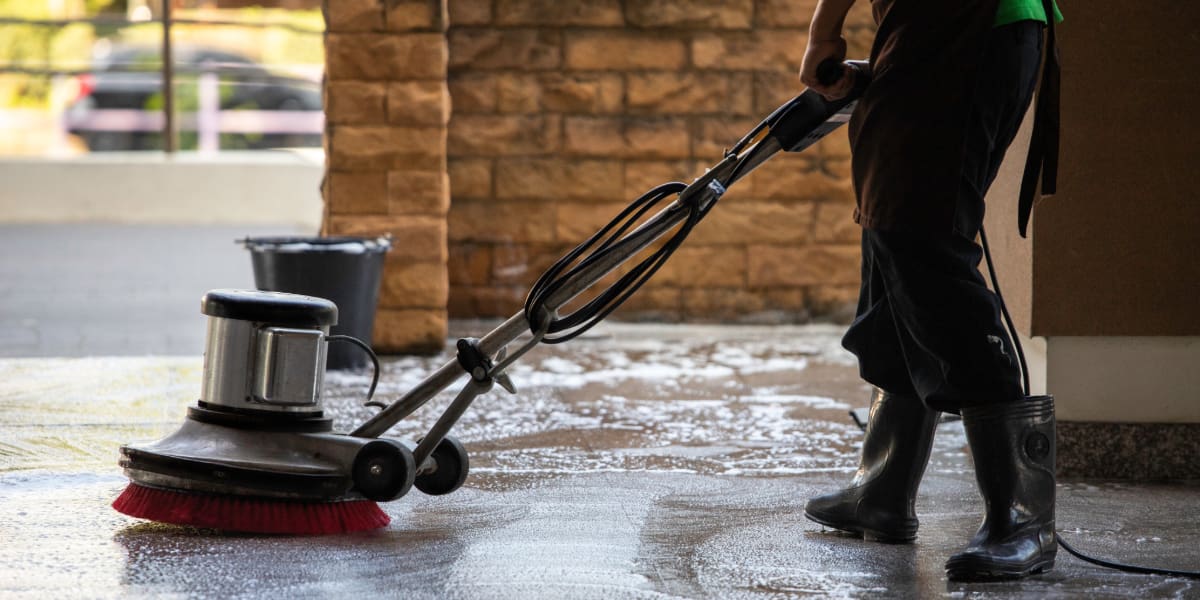Person using a floor scrubber machine as the best cleaner for concrete floors in an indoor area with soap and water on the surface.