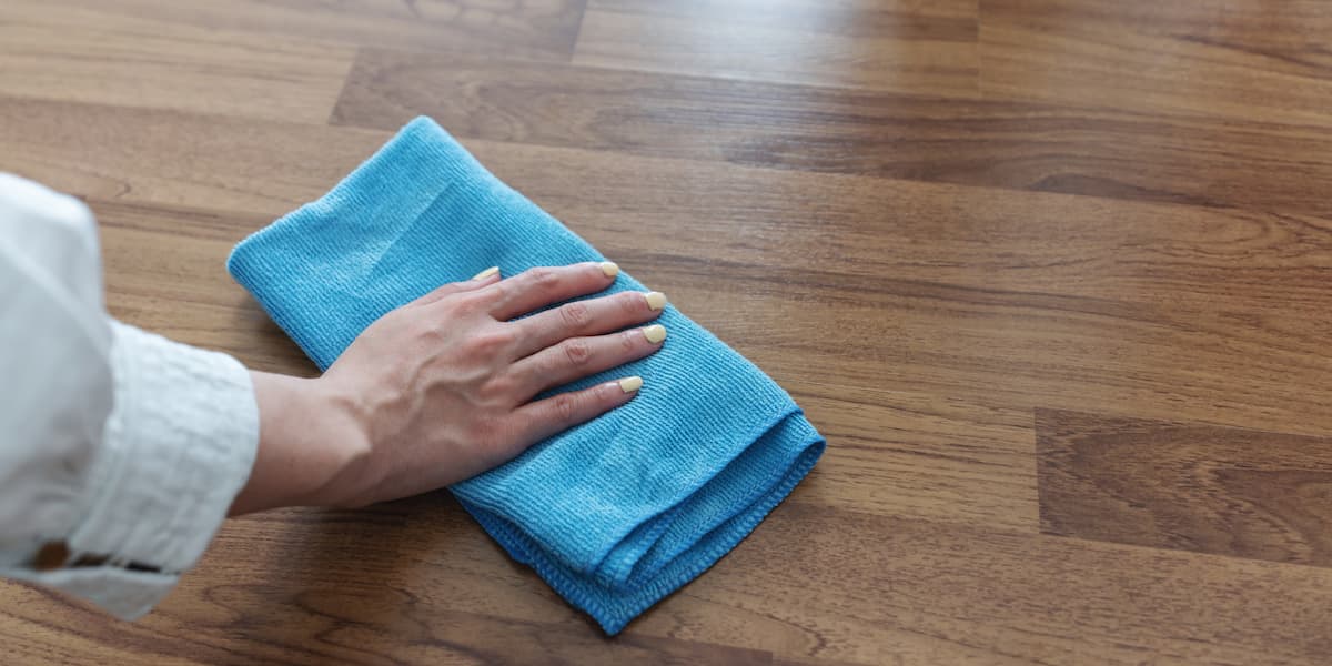 Hand wiping laminate flooring with a microfiber cloth showing how to clean laminate floors safely without damaging the finish